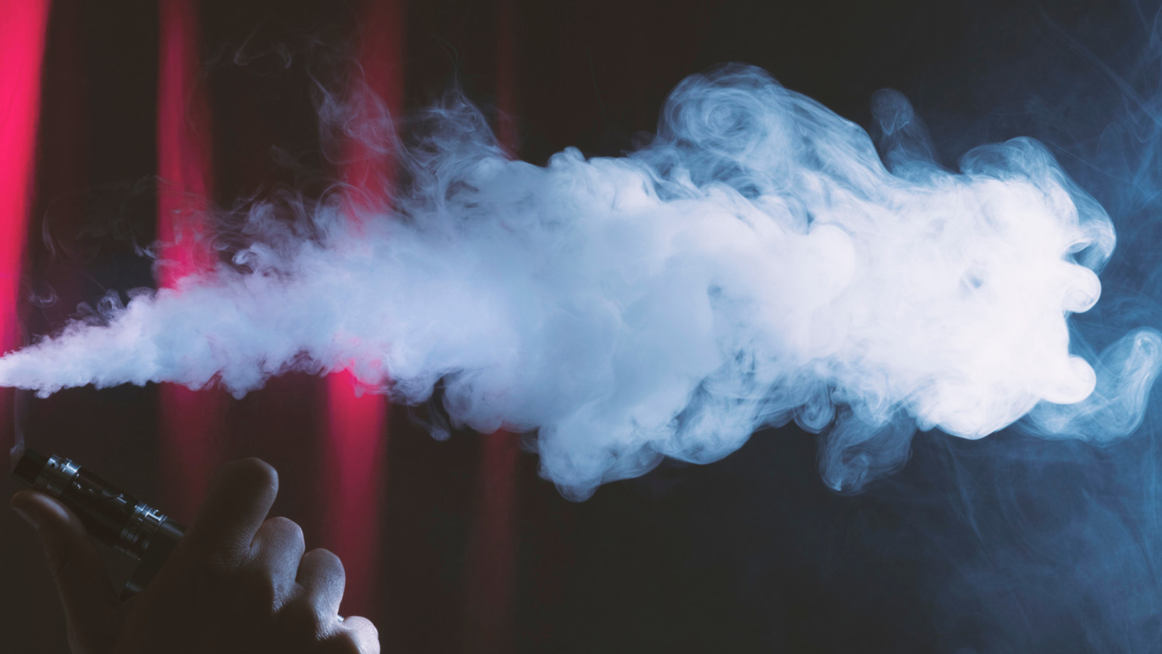 Vapoteur exhalant une vapeur dense devant un fond sombre aux reflets rouges et bleus